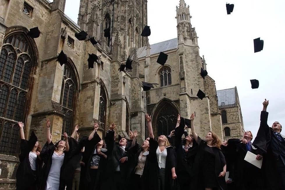 Graduates in gowns throwing their caps in the air outside a gothic cathedral