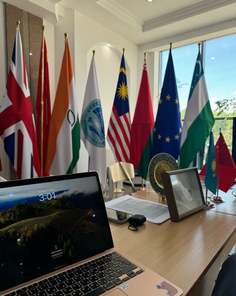 Flags of several countries by a meeting-room window, an open laptop on the table