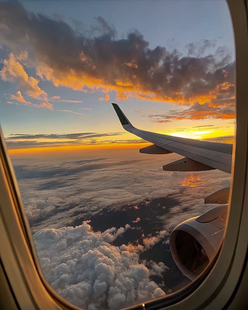 An aircraft wing above the clouds at sunset, seen through the window